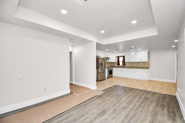 unfurnished living room with a raised ceiling, sink, light wood-type flooring, and ceiling fan