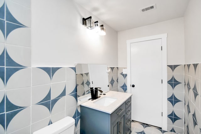 bathroom with toilet, vanity, and tile walls