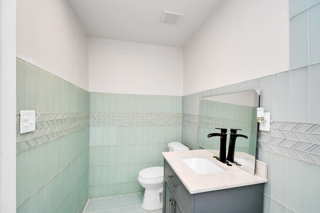 bathroom featuring toilet, vanity, tile walls, and tile patterned flooring