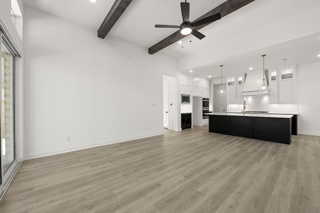 unfurnished living room featuring beamed ceiling, ceiling fan, plenty of natural light, and light hardwood / wood-style floors