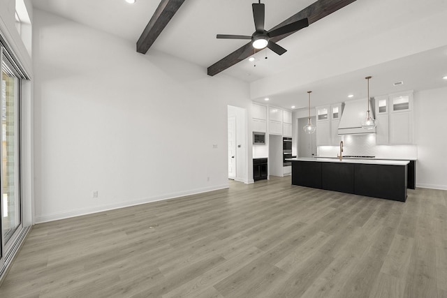 unfurnished living room featuring beamed ceiling, ceiling fan, sink, and light hardwood / wood-style floors