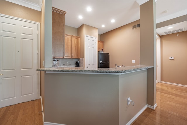 kitchen featuring tasteful backsplash, light stone countertops, kitchen peninsula, light hardwood / wood-style flooring, and black refrigerator