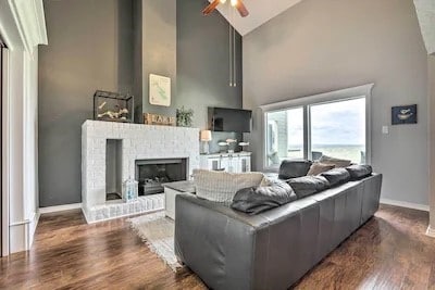 living room featuring dark hardwood / wood-style flooring, ceiling fan, high vaulted ceiling, and a brick fireplace