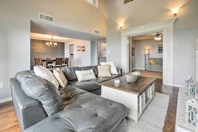 living room featuring wood-type flooring, a high ceiling, and ceiling fan with notable chandelier