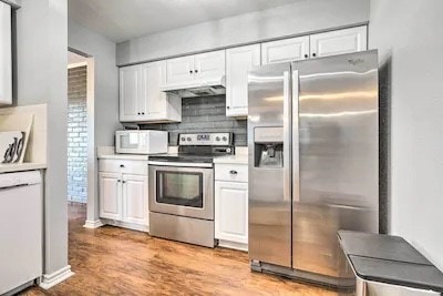 kitchen with stainless steel appliances, tasteful backsplash, light wood-type flooring, and white cabinets