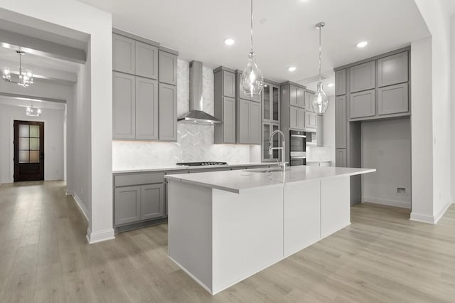 22067 Breakwater Ln, Porter, TX 77365 - kitchen with gray cabinetry, wall chimney range hood, a sink, backsplash, and light wood-type flooring