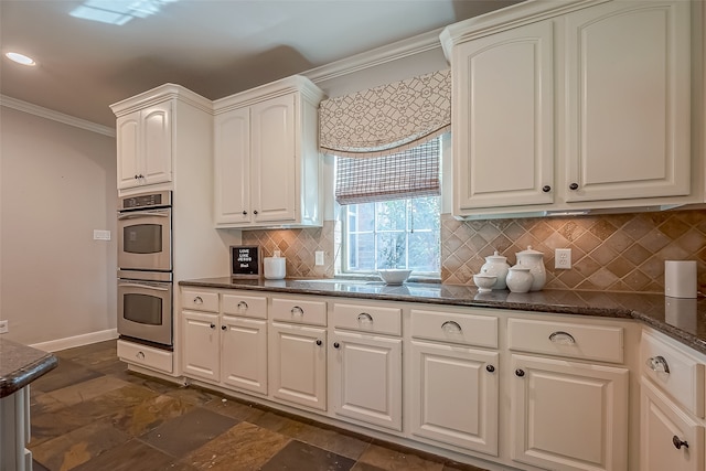 kitchen with dark stone counters, white cabinets, crown molding, double oven, and tasteful backsplash