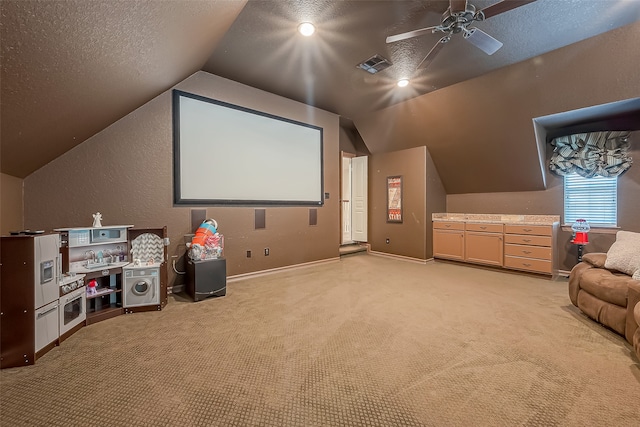 cinema room featuring ceiling fan, light colored carpet, lofted ceiling, and a textured ceiling