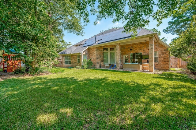 rear view of property featuring solar panels, a yard, and ceiling fan