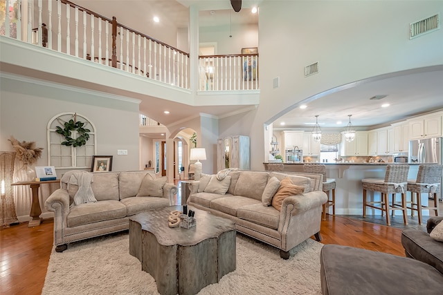 living room with light wood-type flooring, crown molding, and a high ceiling