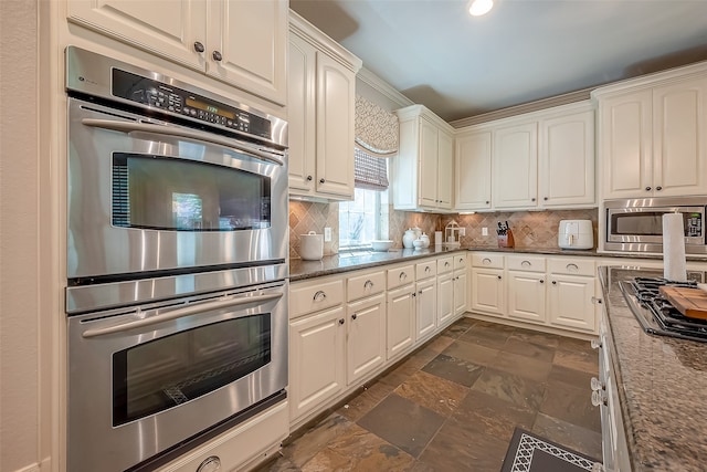 kitchen featuring decorative backsplash, white cabinets, dark stone counters, and appliances with stainless steel finishes