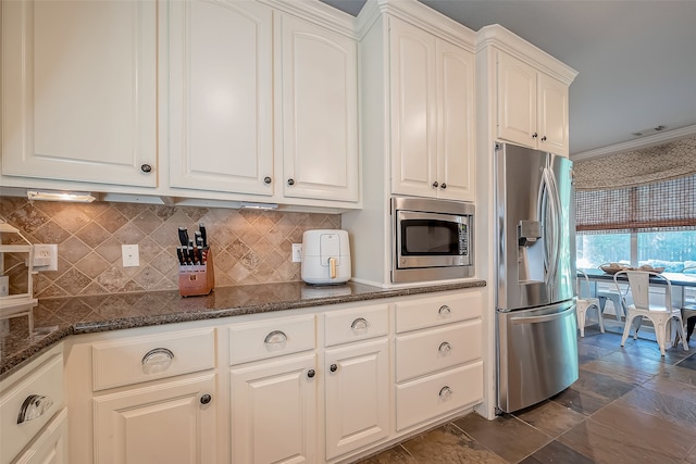 kitchen featuring stainless steel appliances, dark stone countertops, crown molding, decorative backsplash, and white cabinets