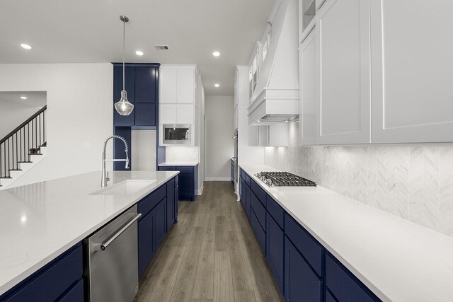 4707 Arbor Park Dr, Manvel, TX 77583 - kitchen with stainless steel appliances, a sink, blue cabinets, custom exhaust hood, and light wood-style floors