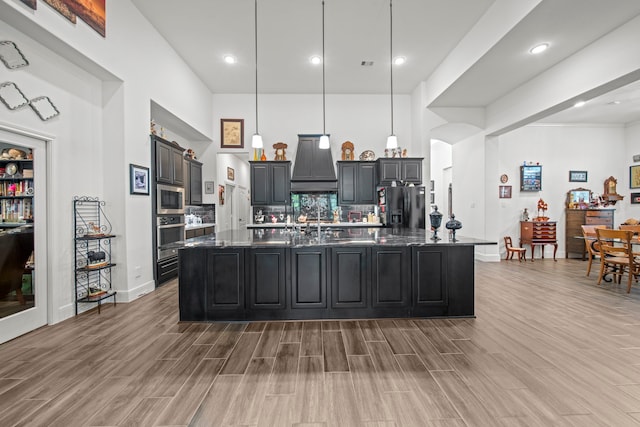 kitchen featuring tasteful backsplash, hanging light fixtures, appliances with stainless steel finishes, a kitchen island with sink, and hardwood / wood-style flooring