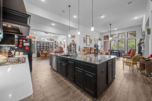 kitchen with ceiling fan, an island with sink, dark stone counters, sink, and decorative light fixtures