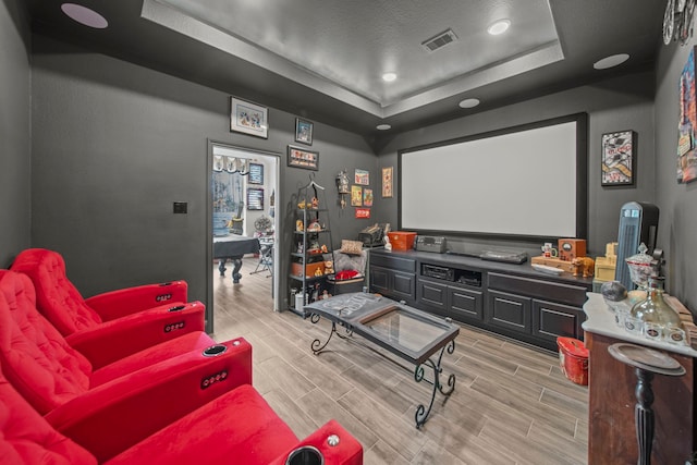 cinema room featuring a raised ceiling, a textured ceiling, and light wood-type flooring