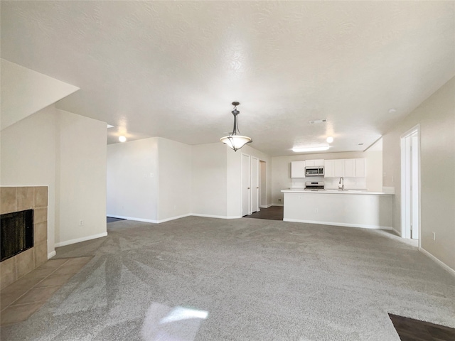 unfurnished living room featuring a textured ceiling, sink, a tile fireplace, and dark carpet