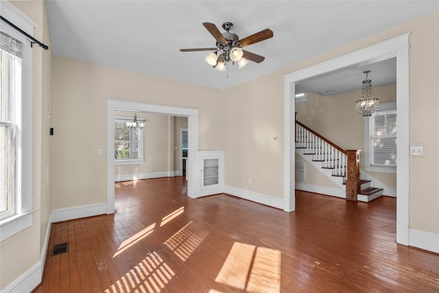 unfurnished living room with ceiling fan with notable chandelier and dark hardwood / wood-style flooring