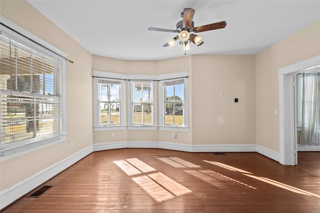 empty room with dark hardwood / wood-style floors, a healthy amount of sunlight, and ceiling fan