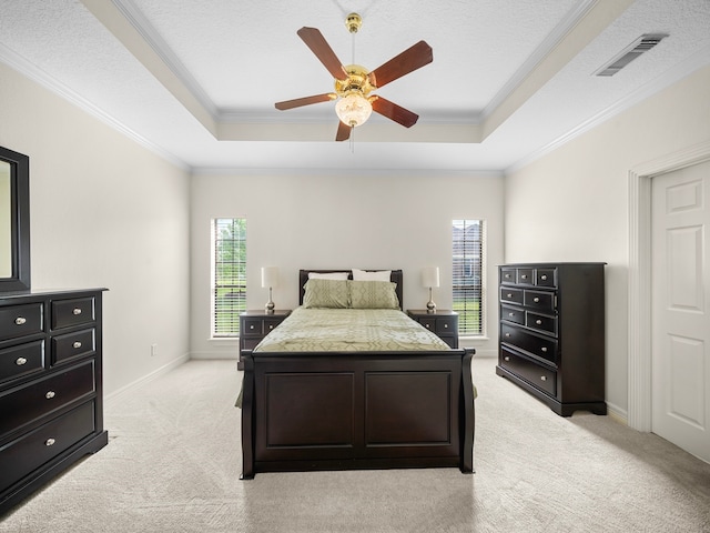 bedroom with light carpet, ceiling fan, a textured ceiling, a tray ceiling, and ornamental molding