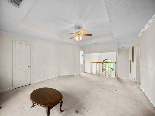 empty room with a raised ceiling, a textured ceiling, ceiling fan, crown molding, and light colored carpet