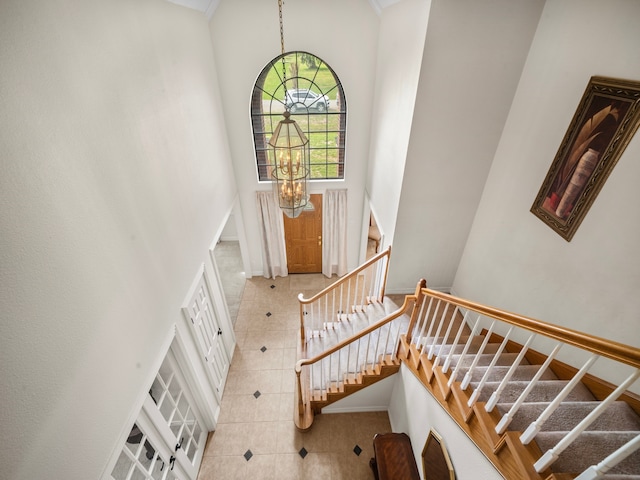 staircase featuring a towering ceiling, an inviting chandelier, and tile patterned flooring