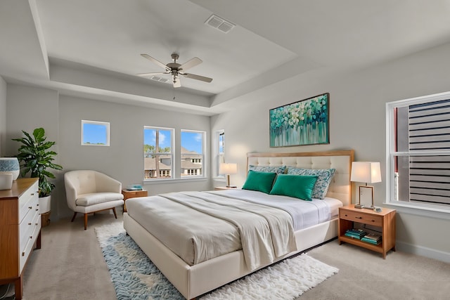 bedroom with visible vents, a ceiling fan, baseboards, a raised ceiling, and light colored carpet