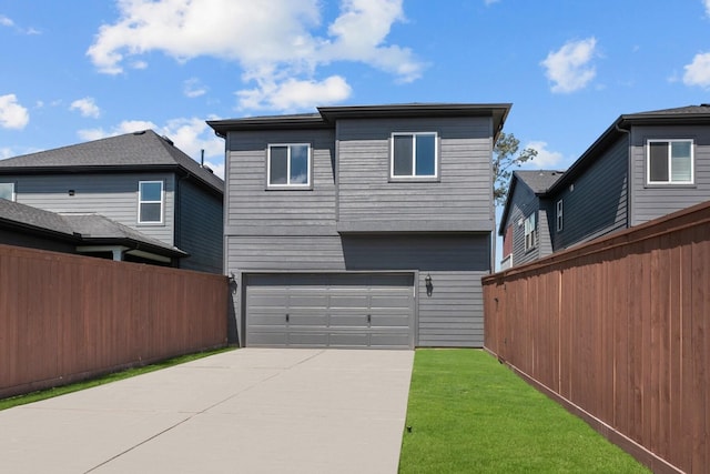 rear view of property featuring concrete driveway, an attached garage, fence, and a yard