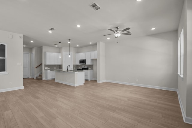 kitchen featuring a sink, stainless steel appliances, open floor plan, light wood-style floors, and tasteful backsplash