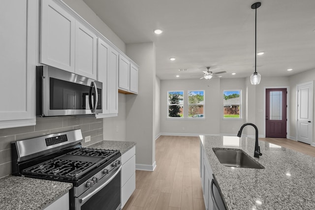 kitchen featuring a sink, stainless steel appliances, white cabinets, light wood-style floors, and tasteful backsplash