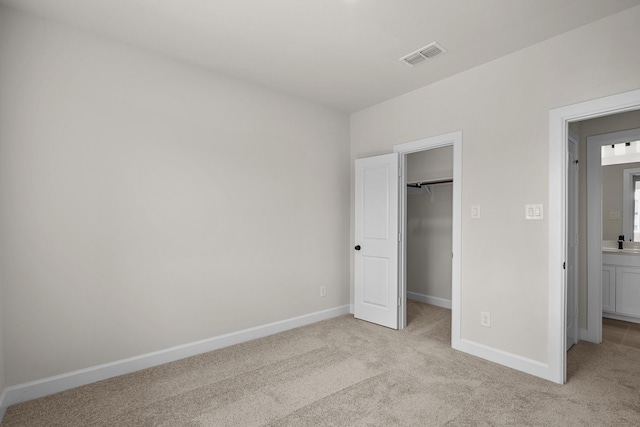 unfurnished bedroom featuring visible vents, light carpet, baseboards, and a walk in closet