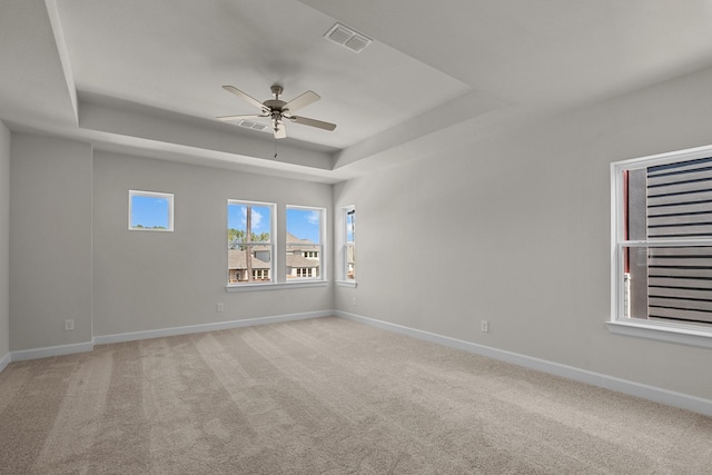 spare room with visible vents, a raised ceiling, a ceiling fan, baseboards, and light colored carpet