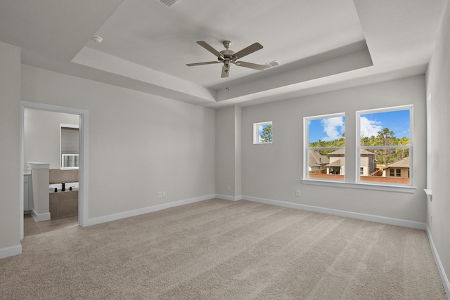 carpeted spare room with ceiling fan, a raised ceiling, and baseboards