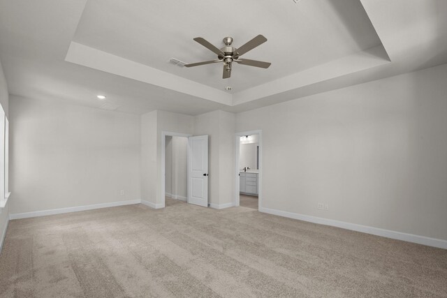 unfurnished bedroom featuring light carpet, ensuite bath, a raised ceiling, and baseboards