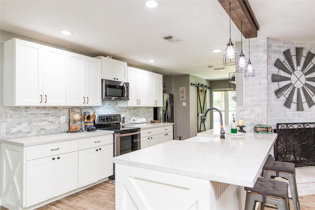 kitchen featuring appliances with stainless steel finishes, a breakfast bar area, white cabinets, pendant lighting, and sink