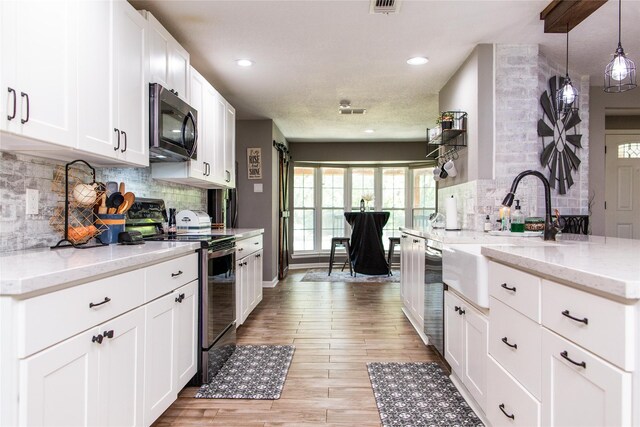 kitchen with appliances with stainless steel finishes, white cabinetry, light hardwood / wood-style floors, pendant lighting, and light stone counters