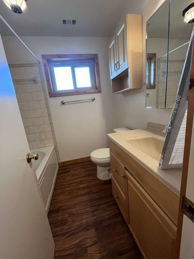 full bathroom with vanity, toilet, tiled shower / bath, and hardwood / wood-style floors