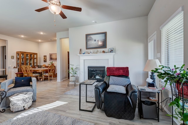 living room with a tile fireplace, light hardwood / wood-style floors, and ceiling fan