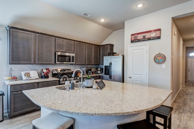 kitchen featuring light wood-type flooring, appliances with stainless steel finishes, a kitchen bar, and a kitchen island with sink