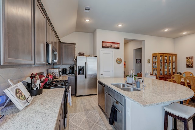 kitchen featuring an island with sink, sink, light stone countertops, vaulted ceiling, and appliances with stainless steel finishes