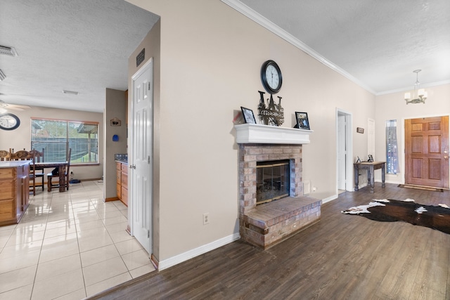 living room with ceiling fan with notable chandelier, a fireplace, a textured ceiling, light hardwood / wood-style floors, and crown molding