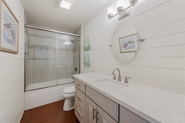 full bathroom featuring a textured ceiling, shower / bath combination with glass door, toilet, vanity, and wooden walls