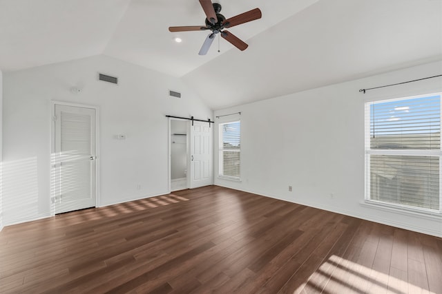 spare room featuring dark hardwood / wood-style floors, a barn door, ceiling fan, and vaulted ceiling