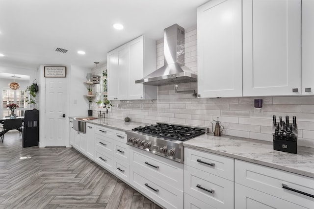 kitchen with stainless steel gas stovetop, white cabinetry, light parquet flooring, wall chimney exhaust hood, and sink