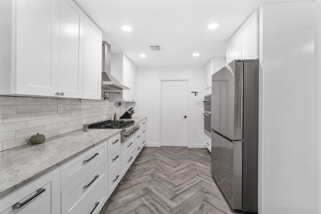 kitchen featuring appliances with stainless steel finishes, wall chimney exhaust hood, white cabinetry, and light stone countertops