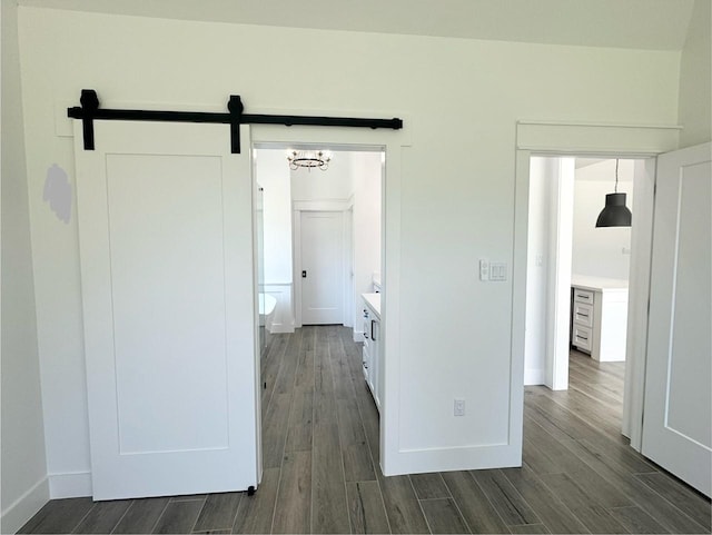 corridor featuring dark wood-type flooring, baseboards, and a barn door