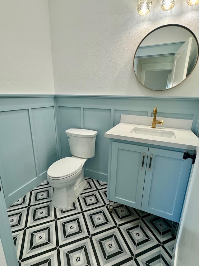 half bathroom with a wainscoted wall, vanity, and toilet