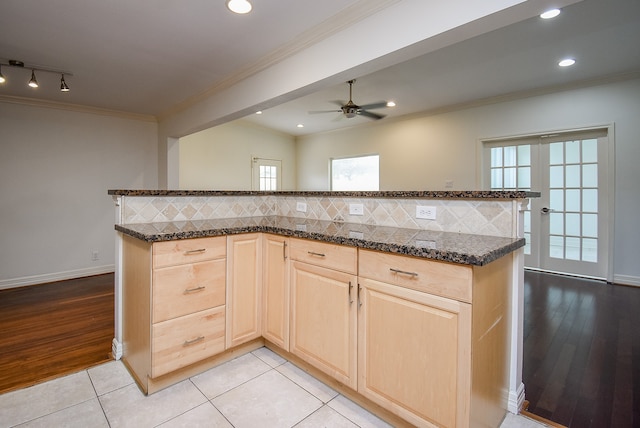 kitchen featuring dark stone countertops, tasteful backsplash, light brown cabinetry, and light wood-type flooring