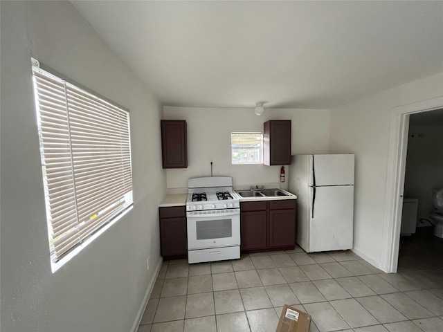 kitchen with sink, dark brown cabinetry, white appliances, and light tile patterned floors