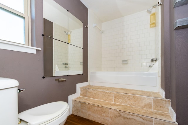 bathroom with hardwood / wood-style floors, toilet, and tiled shower / bath